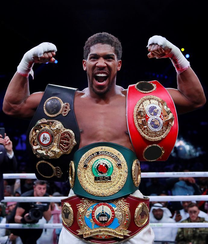 Anthony Joshua poses with his belts inside the boxing ring