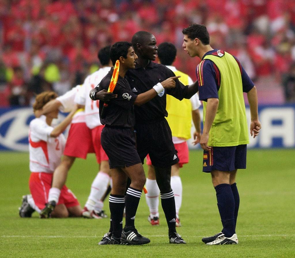 Albert Luque of Spain argues with Assistant Referees Ali Tomusange and Michael Ragoonath