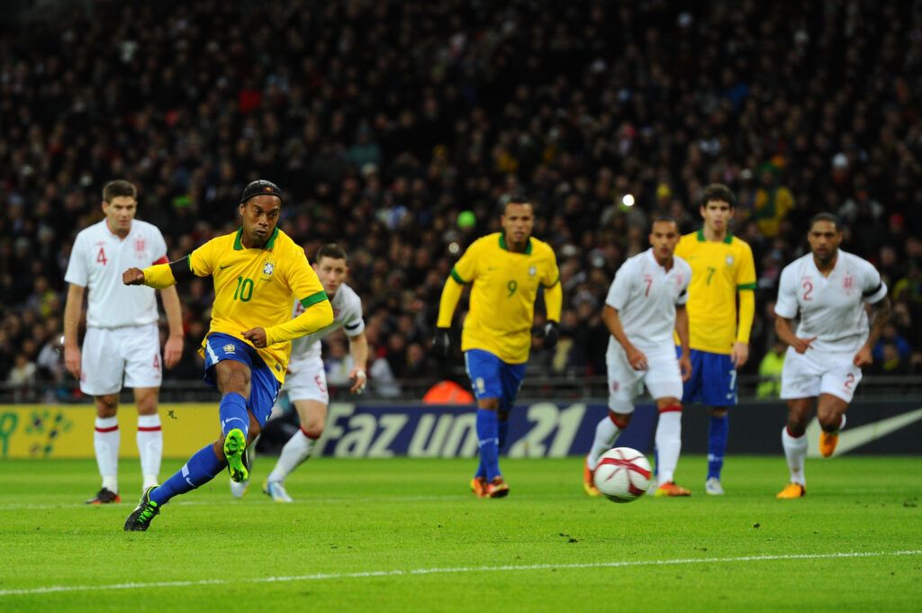 O brasileiro Ronaldinho bate um pênalti, que foi defendido pelo inglês Joe Hart